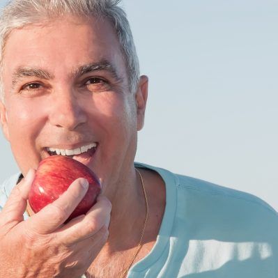 Bărbat care mușcă dintr-un măr roși și delicios, cu implant dentar este posibil din nou