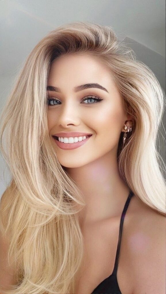 femeie cu păr blond și lung, maieu negru și decoltat, zâmbet perfect cu fațete dentare