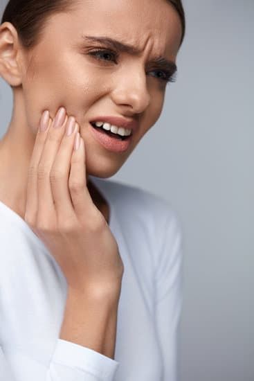 femeie brunetă, cu durere dentară, ținându-se de obraz, scapă de infecția dentară cu rezecția apicală